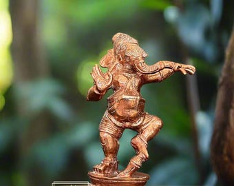 May include: A copper-colored statue of Ganesha, the Hindu god of wisdom and prosperity, standing on a circular base. The statue is intricately detailed and depicts Ganesha in a dancing pose.