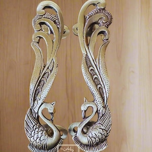 May include: A pair of ornate, silver-toned door handles shaped like swans with their necks intertwined. The handles are intricately detailed with a floral design and have a textured finish.