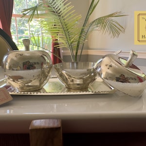 Puede incluir: Platos de servir de plata en forma de manzana con un taz&oacute;n en una bandeja de plata. Los platos son parte de un juego con una etiqueta que dice "The Golden Heritage".