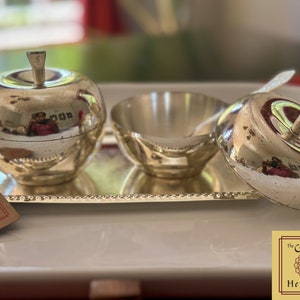 Puede incluir: Azucarero de plata en forma de manzana con tapa y un cuenco de plata a juego en una bandeja de plata. La bandeja tiene un borde de cuentas. El conjunto est&aacute; etiquetado como "The Golden Heritage".