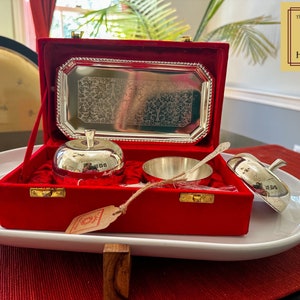 Puede incluir: Un plato de plata con forma de manzana con tapa, un cuenco de plata y una cuchara de plata se muestran en una caja de terciopelo rojo con cierre dorado. La caja est&aacute; abierta y los art&iacute;culos son visibles. La caja est&aacute; sentada sobre una bandeja ovalada blanca. El texto "The Golden Heritage" es visible en una etiqueta dorada.