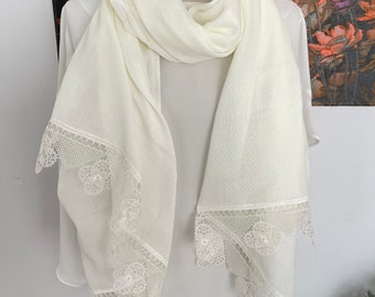 May include: A white scarf with a delicate lace trim. The lace is a floral pattern and is white.