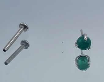 May include: Two surgical steel body jewelry pieces. One is a straight barbell with a flat end. The other is a curved barbell with a green gemstone.