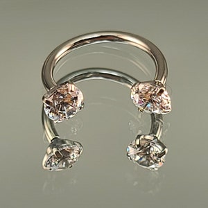 May include: A silver circular barbell with two clear crystal gems on each end.