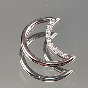 May include: Silver crescent moon septum ring with clear cubic zirconia stones.