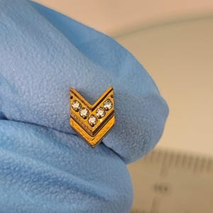 May include: Gold chevron shaped body jewelry with five clear rhinestones.