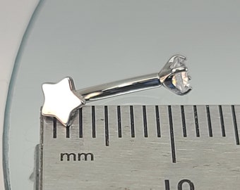 Può includere: Gioiello per il corpo a forma di barra in argento con un'estremità a forma di stella e un gioiello trasparente all'altra estremità. La barra viene misurata con un righello.