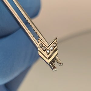 May include: A silver arrow-shaped charm with five clear cubic zirconia stones set in the center.