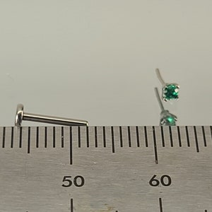 May include: Two silver nose rings with green gemstones. The rings are measured on a ruler with markings in centimetres.