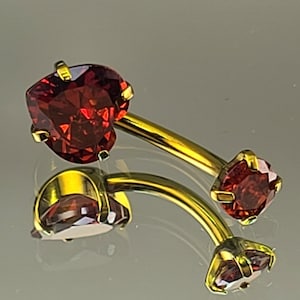 May include: A gold belly button ring with two red heart-shaped gems. The ring is curved and has a small ball on the end.
