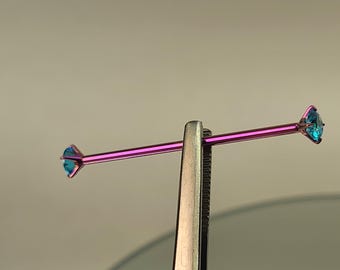 May include: A purple industrial barbell piercing held by tweezers. Each end of the barbell features a teal-colored, diamond-shaped gem. The jewelry is displayed against a neutral background.