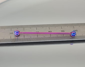 May include: A pink titanium barbell with blue opal ends, measured against a ruler. The barbell is approximately 3.5 cm long.