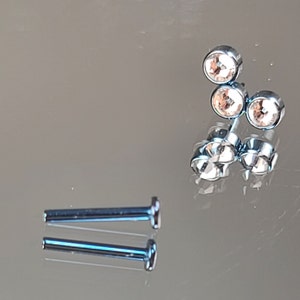 May include: A set of three clear crystal stud earrings with a silver post and back. The earrings are arranged in a triangle shape.