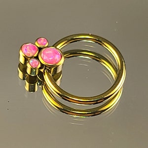 May include: A gold-toned body jewelry ring with a cluster of pink opal stones. The ring is double-looped and has a smooth finish.