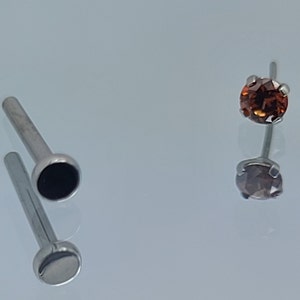 May include: Two nose rings with different colored gems. One ring has a black gem and the other has a brown gem.