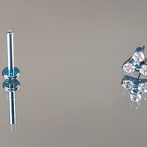 May include: A blue barbell with a clear gem top. The gem top has three clear stones in a triangular shape.