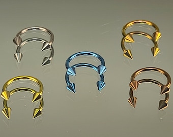 May include: Five pairs of surgical steel body jewelry with pointed ends. The jewelry is available in silver, gold, and blue.