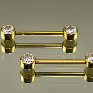 May include: Two gold-colored barbell body jewelry pieces with clear round gemstones on each end.
