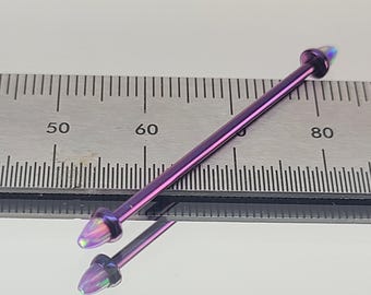 May include: A purple industrial barbell piercing with iridescent cone-shaped ends. The barbell is approximately 3 inches long. The jewelry is shown on a reflective surface next to a ruler, highlighting its length.