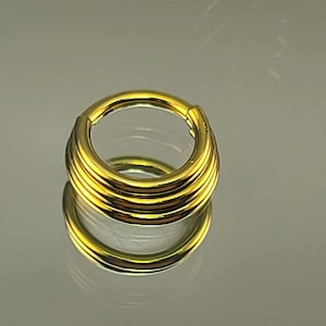 May include: Gold-toned body jewelry with a layered design. The ring is made of multiple bands that are stacked on top of each other. The ring is a seamless hoop.