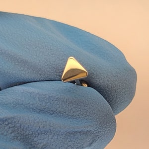 May include: A gold triangle shaped nose piercing stud.
