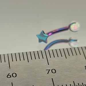 May include: A close-up of a rainbow-coloured star and opal body jewellery. The jewellery is measured against a ruler, showing it is approximately 7 cm long.