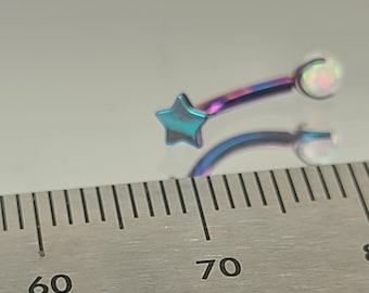 Puede incluir: Primer plano de una joya para el cuerpo en forma de estrella y ópalo con colores arcoíris. La joya se mide con una regla, mostrando que mide aproximadamente 7 cm de largo.