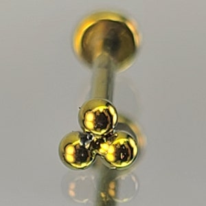 May include: Gold body jewelry with a three-ball design. The balls are round and have a shiny finish.