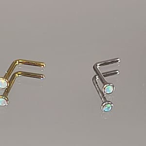 May include: Four nose rings with opal stones. The rings are made of different metals: blue, gold, silver, and gold. The rings are all L-shaped.