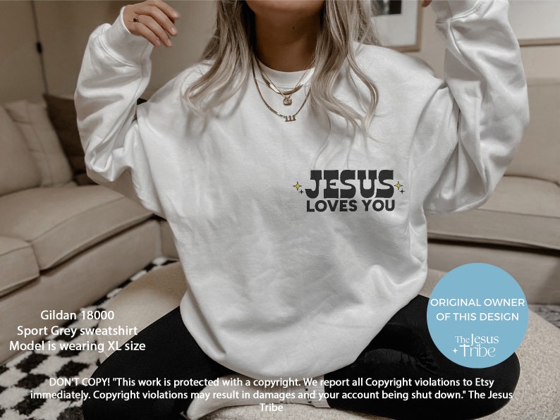 K&ouml;nnte beinhalten: Ein wei&szlig;es Gildan 18000 Sport Grey Sweatshirt mit dem Text "JESUS LOVES YOU" in Schwarz. Der Text wird von Stern-Grafiken begleitet. Das Sweatshirt ist ein l&auml;ssiges Kleidungsst&uuml;ck f&uuml;r den Alltag.