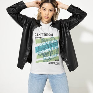 May include: White t-shirt with a graphic of a tiger's face and the text "Can't Throw Stones While Washing Feet John 13:14".