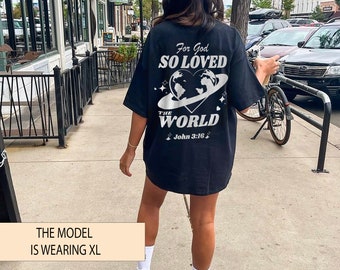 May include: Black t-shirt with a white graphic design featuring a heart with a globe inside and the text "For God So Loved The World John 3:16". The model is wearing a size XL.