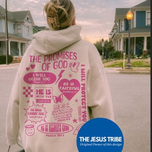 May include: Sand-colored hoodie with pink text and graphics. The back of the hoodie features the text "THE PROMISES OF GOD" and various Bible verses. The design includes hearts, a dove, a butterfly, and other decorative elements. The brand logo "THE JESUS TRIBE" is at the bottom.