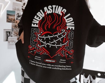 May include: Black sweatshirt with a graphic design featuring a heart pierced with thorns and flames, with the words "EVERLASTING LOVE" in white. The text "Always Forever" and a Bible verse are also printed on the shirt.