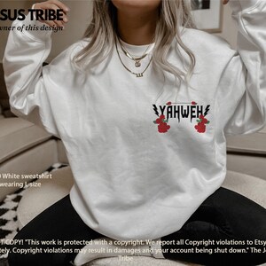 May include: White sweatshirt featuring the text "YAHWEH" in black with red roses on either side. The text is in a bold, gothic font. The sweatshirt is a Gildan 18000 and the model is wearing a size L.