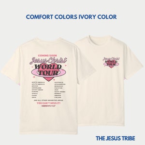 Puede incluir: Una camiseta beige con un gr&aacute;fico de coraz&oacute;n rosa y el texto "Jesus Christ World Tour" en la espalda. La parte delantera de la camiseta tiene una versi&oacute;n m&aacute;s peque&ntilde;a del gr&aacute;fico en el pecho izquierdo. El texto "The Jesus Tribe" est&aacute; impreso en la parte inferior de la camiseta.