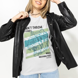May include: White unisex t-shirt with a graphic print of a tiger's face and the text "Can't Throw Stones While Washing Feet John 13:14".