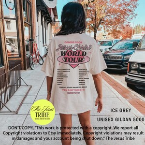 Puede incluir: Una camiseta blanca con un dise&ntilde;o gr&aacute;fico rosa que dice "Jesus Christ World Tour" con un coraz&oacute;n rosa y un c&iacute;rculo rosa alrededor. La camiseta tambi&eacute;n tiene una lista de pa&iacute;ses y el texto "You Can't Miss It! Hebrews 9:27". La camiseta est&aacute; puesta en una modelo frente a un edificio de ladrillo. El texto "The Jesus Tribe" est&aacute; en un c&iacute;rculo amarillo debajo de la modelo. El texto "ICE GREY UNISEX GILDAN 5000" est&aacute; debajo del c&iacute;rculo amarillo. El texto "DON'T COPY! "This work is protected with a copyright. We report all Copyright violations to Etsy immediately. Copyright violations may result in damages and your account being shut down." The Jesus Tribe" est&aacute; en la parte inferior de la imagen.
