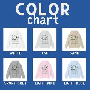 K&ouml;nnte beinhalten: Farbkarte mit sechs verschiedenen Farboptionen f&uuml;r einen Hoodie. Der Hoodie hat einen grafischen Druck eines Globus mit dem Text "For God so Loved the World". Die gezeigten Farben sind Wei&szlig;, Asche, Sand, Sportgrau, Hellrosa und Hellblau.
