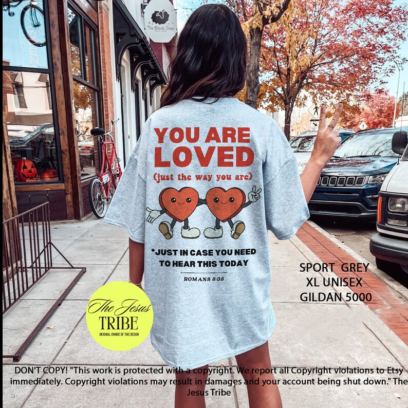 K&ouml;nnte beinhalten: Ein hellgraues T-Shirt mit dem Text "You Are Loved (just the way you are)" und zwei Comic-Herzen, die sich an den H&auml;nden halten. Der Text "Just in case you need to hear this today" befindet sich unter den Herzen, mit dem Schriftzitat "R&ouml;mer 8:38" darunter. Das T-Shirt hat auch den Text "Sport Grey XL Unisex Gildan 5000" in der unteren rechten Ecke.
