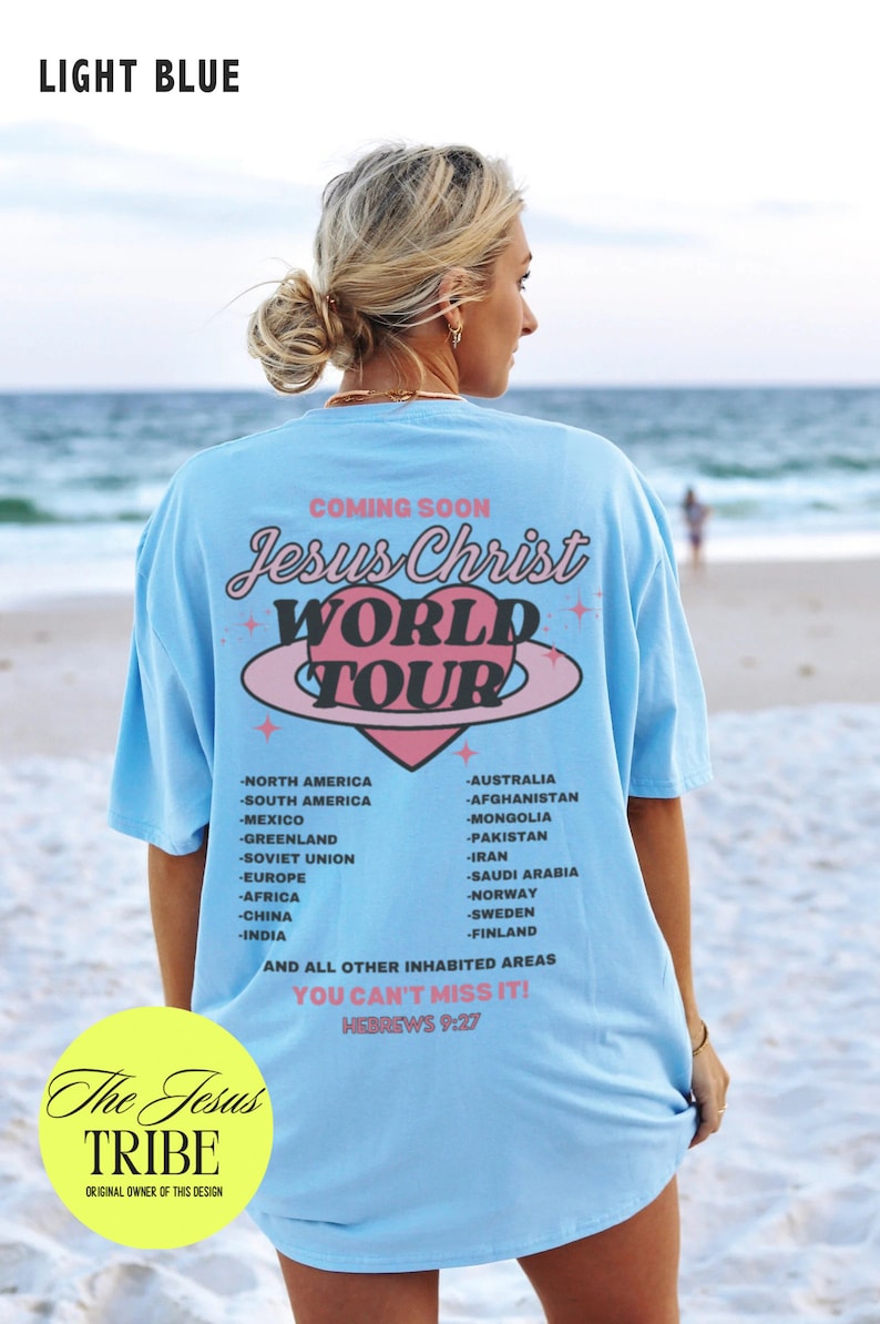Puede incluir: Una camiseta azul claro con un gr&aacute;fico de coraz&oacute;n rosa y el texto "Jesus Christ World Tour" impreso en la espalda. El texto "You Can't Miss It! Hebrews 9:27" tambi&eacute;n est&aacute; impreso en la camiseta. La camiseta la lleva puesta una persona de pie en una playa.
