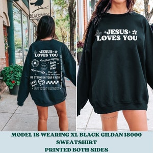 May include: Black sweatshirt with white text and graphics. The front reads "+JESUS+* LOVES YOU" with a butterfly and flower. The back has additional text including "BE THE LIGHT" and "BE STRONG IN YOUR FAITH".
