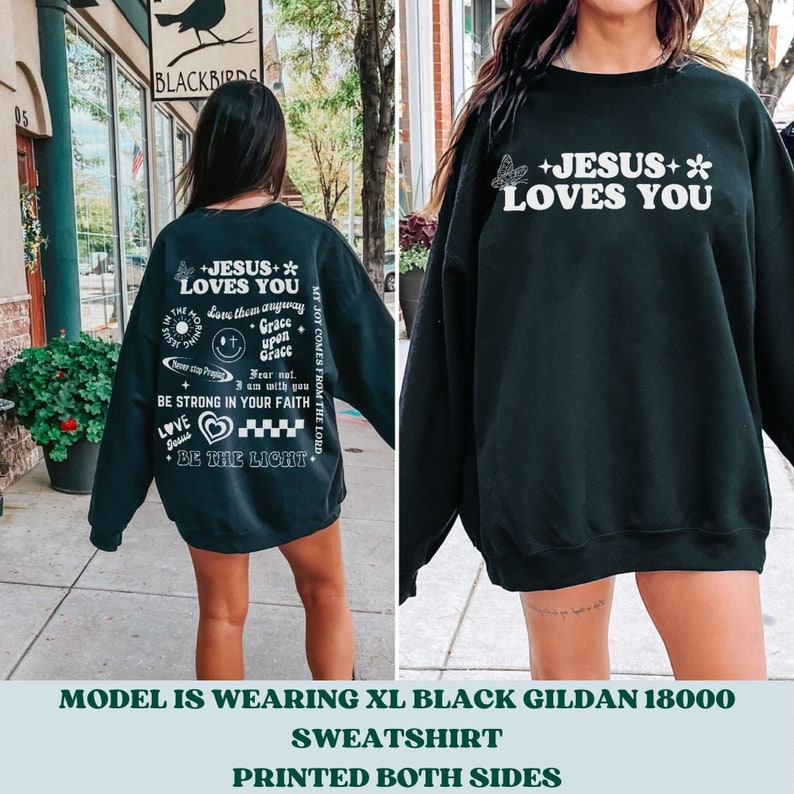 May include: Black sweatshirt with white text and graphics. The front reads "+JESUS+* LOVES YOU" with a butterfly and flower. The back has additional text including "BE THE LIGHT" and "BE STRONG IN YOUR FAITH".