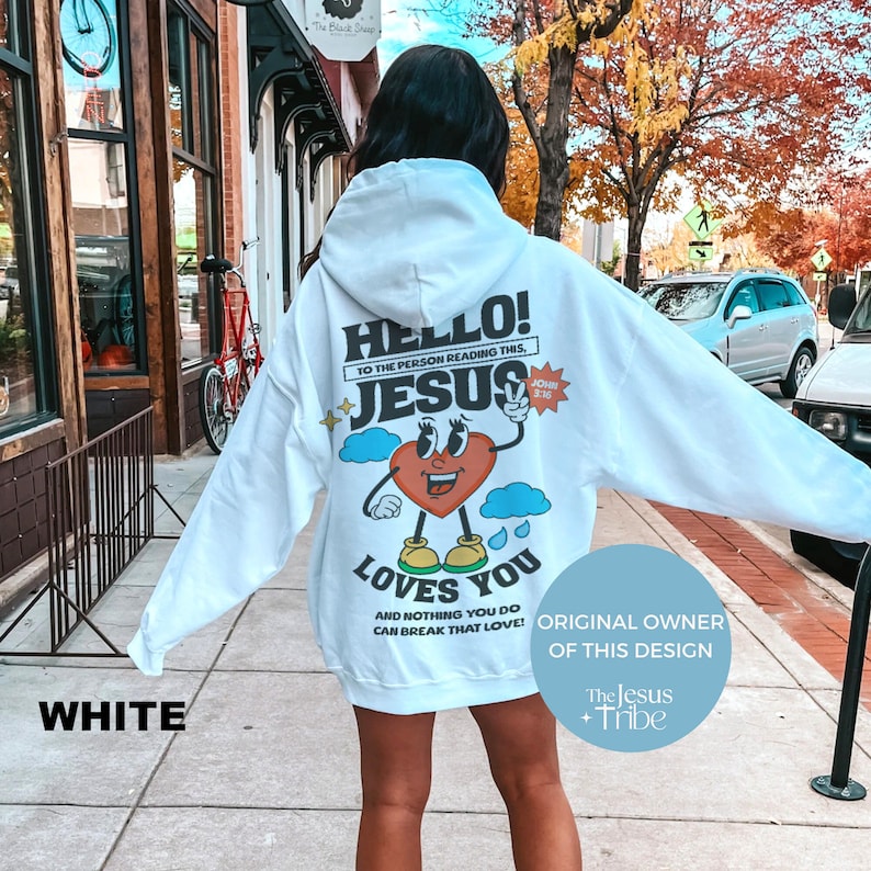 May include: White hoodie with a cartoon heart design and the text "HELLO! TO THE PERSON READING THIS, JESUS LOVES YOU AND NOTHING YOU DO CAN BREAK THAT LOVE!"  The design also includes the text "JOHN 3:16" and a cloud with raindrops. The hoodie has a hood and a pouch pocket. The text "ORIGINAL OWNER OF THIS DESIGN" is on a blue background with the text "The Jesus Tribe" below it.