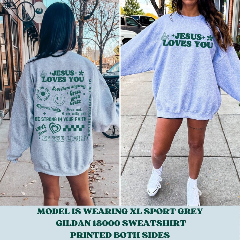 May include: A light grey sweatshirt with the text "+JESUS+ LOVES YOU" in green. The back of the sweatshirt has additional green text and graphics. The sweatshirt is a Gildan 18000 model and is printed on both sides.