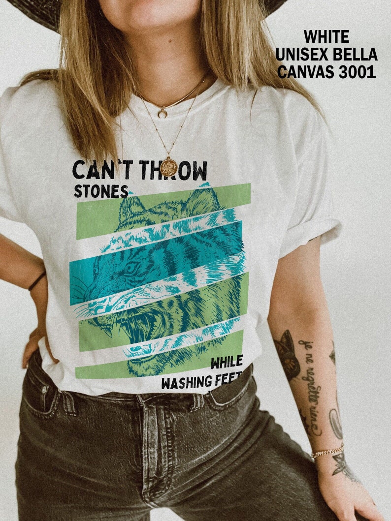 May include: White t-shirt with a green and blue tiger graphic and the text "Can't Throw Stones While Washing Feet".
