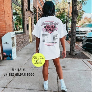 Puede incluir: Una camiseta blanca unisex con un dise&ntilde;o gr&aacute;fico rosa y azul que dice "Jesus Christ World Tour" y enumera pa&iacute;ses. El texto "The Jesus Tribe" est&aacute; en un c&iacute;rculo amarillo en la esquina inferior izquierda. La camiseta es talla XL y es una Gildan 5000.