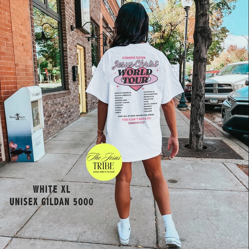 Puede incluir: Una camiseta blanca unisex con un dise&ntilde;o gr&aacute;fico rosa y azul que dice "Jesus Christ World Tour" y enumera pa&iacute;ses. El texto "The Jesus Tribe" est&aacute; en un c&iacute;rculo amarillo en la esquina inferior izquierda. La camiseta es talla XL y es una Gildan 5000.