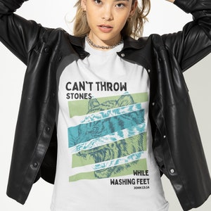 May include: White t-shirt with a graphic print of a tiger's face and the text "Can't Throw Stones While Washing Feet John 13:14".