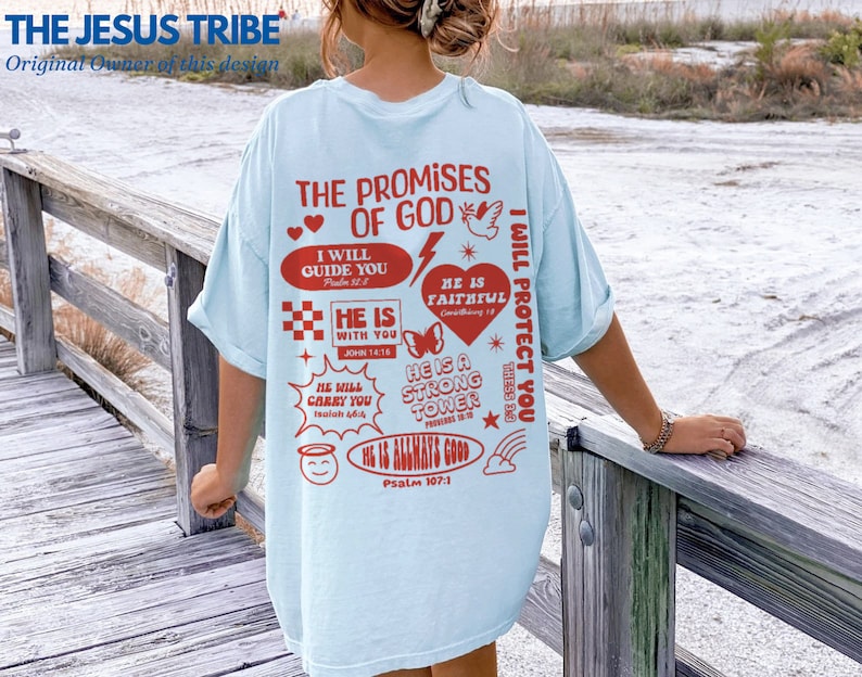 May include: Light blue t-shirt with a graphic print of religious quotes and symbols in red. The text includes "The Promises of God", "I Will Guide You", "He Is With You", "He Is Faithful", "He Is A Strong Tower", "I Will Protect You", and "He Is Always Good".